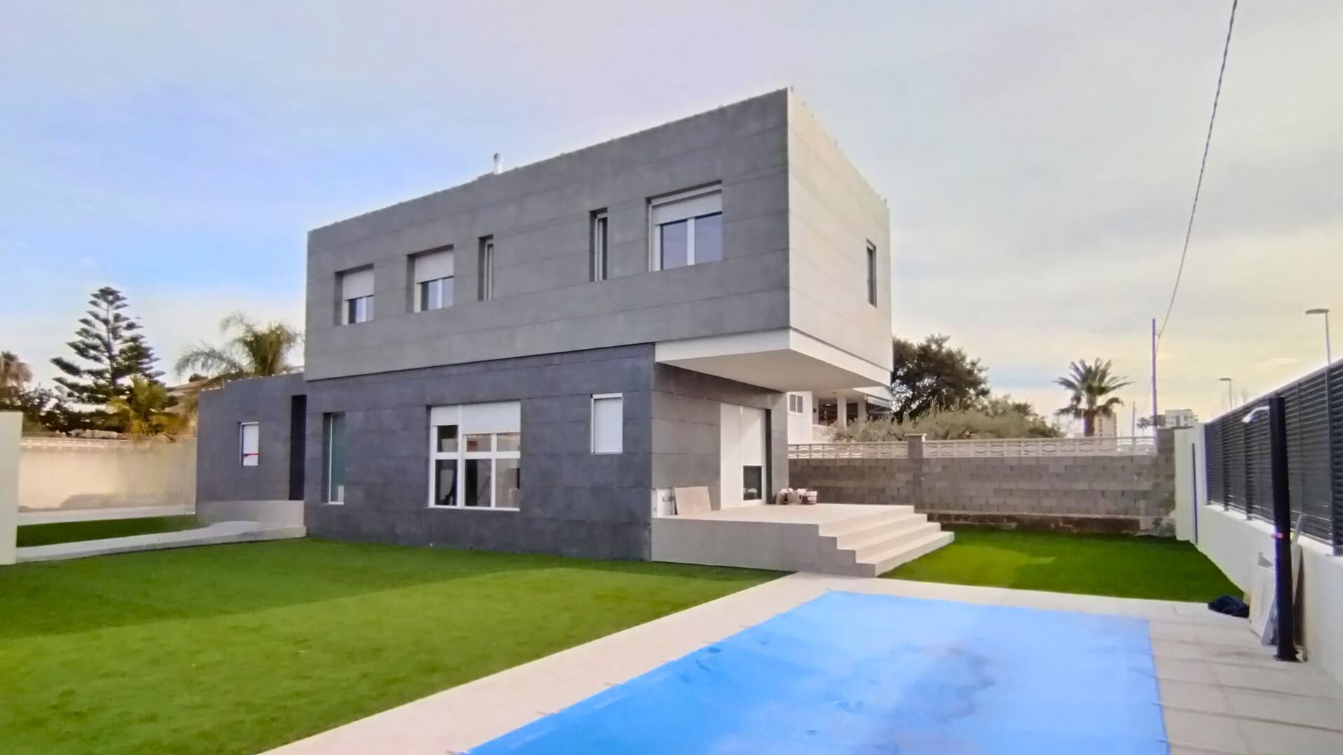 Proyecto de EMBuildings: Casa de arquitectura moderna con revestimiento gris oscuro, grandes ventanales y piscina exterior.